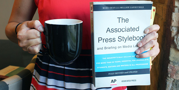 A woman holds a mug of coffee and a book titled, "The Associated Press Stylebook."