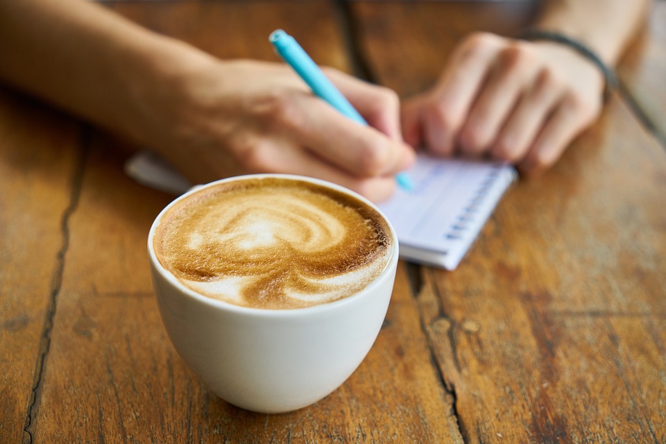 A person writes in a notebook next to a latte