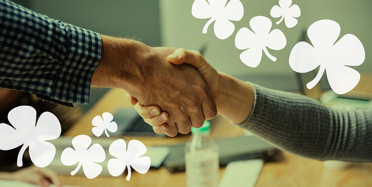 Two people shake hands while four leaf clovers surround the image.