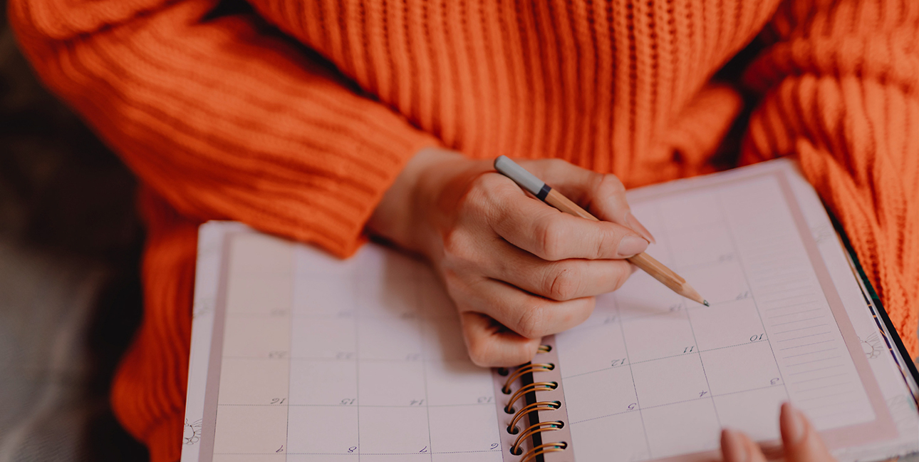 A person in an orange sweater holds a pencil and writes in a journal.
