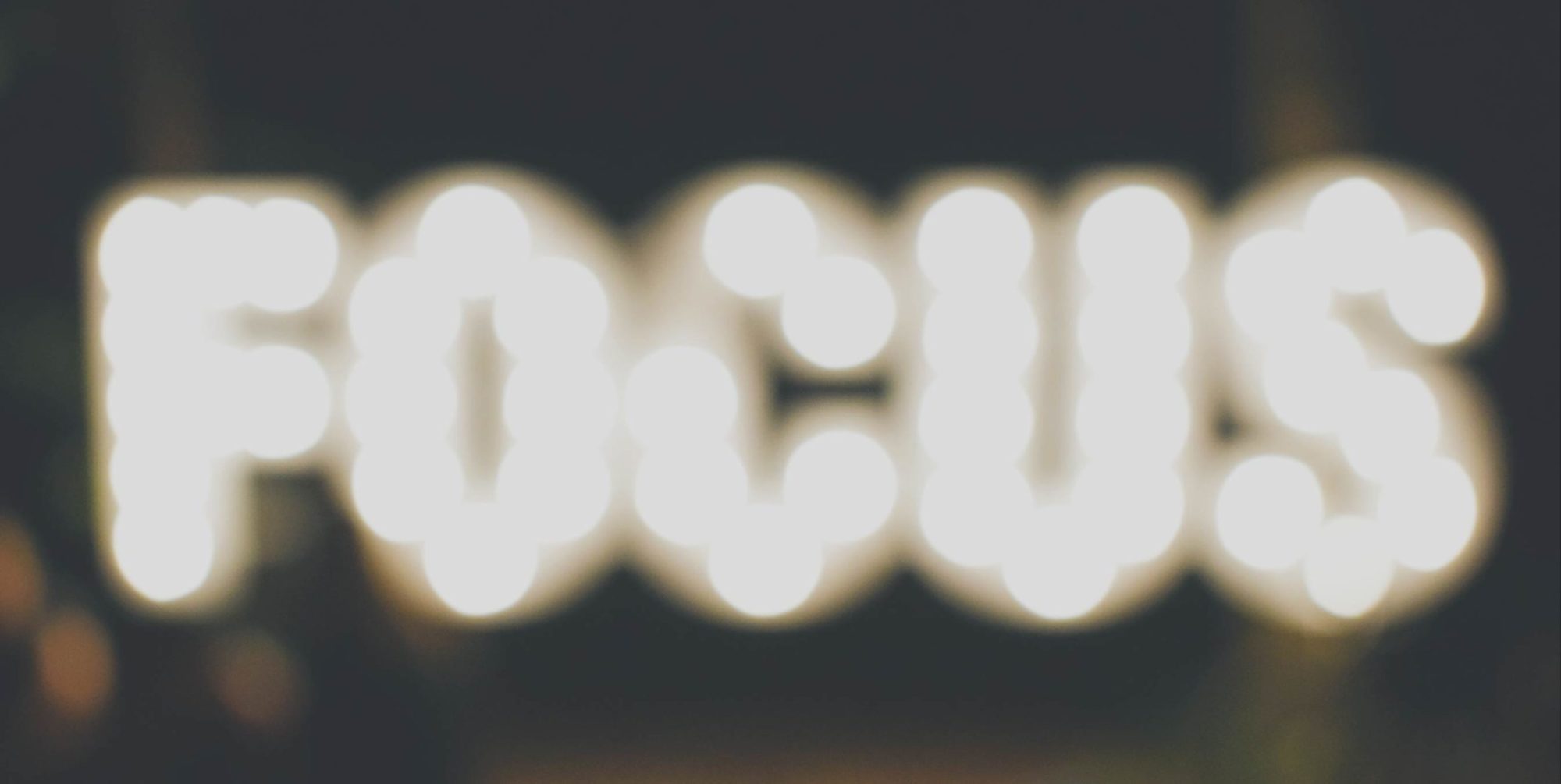 A photo of a lighted sign that reads "FOCUS", and is slightly out of focus.