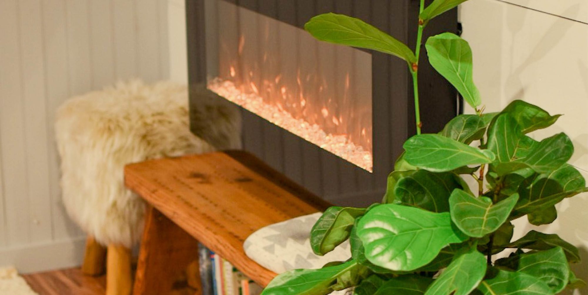 An image of a plant and fuzzy stool next to a fireplace.