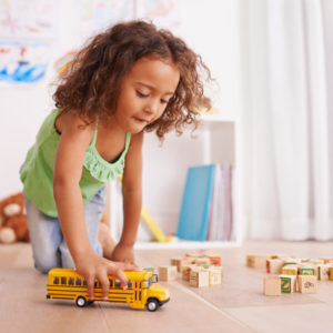 A young girl playing with a toy school bus