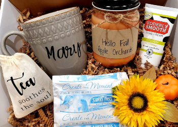 A fall care package with a mug, candle, tea, and flowers.
