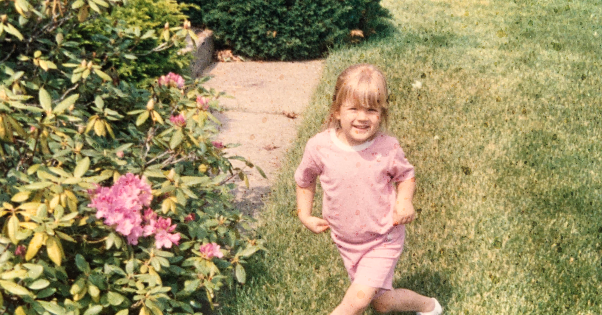Meg Chittenden as a child in a pink shirt crossing her legs by flowers